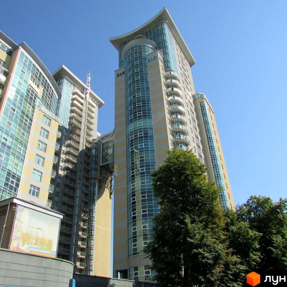 Житловий комплекс Тріумф: високі будівлі з великими вікнами та балконами, оточені зеленими деревами під блакитним небом.