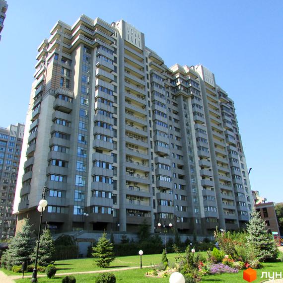 Житловий комплекс Новопечерські Липки: багатоповерховий будинок сірого кольору з балконами. Доглянута прибудинкова територія з зеленими насадженнями та квітами.