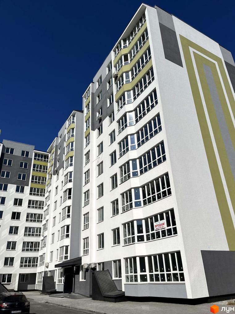 Багатоповерхова новобудова по вул. Тараскова, 5 з білим фасадом, сірими та світло-зеленими елементами. На вікнах є оголошення про продаж.