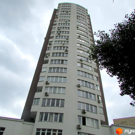 Висотний будинок житлового комплексу Вертикаль з великими вікнами. Прибудинкова територія з зеленими насадженнями.