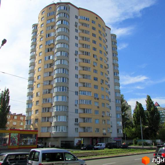 Житловий комплекс на вул. Автозаводська, 29а, з круглою архітектурою та балконами. Прибудинкова територія з зеленими насадженнями та автомобілями.