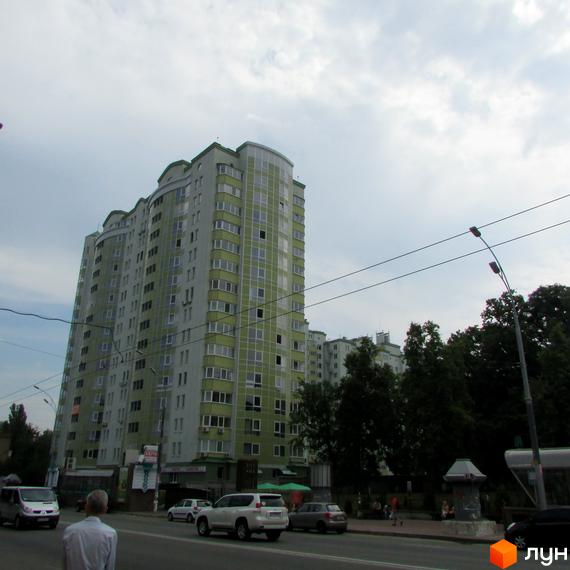 Житловий комплекс Васильківський з сучасним фасадом та зеленими елементами. Прибудинкова територія з автомобілями та зеленими насадженнями.