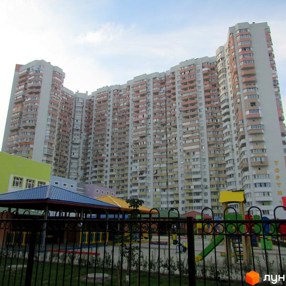 Багатоповерховий житловий комплекс на вул. Драгоманова, 6/1 світло-сірого кольору з численними рожевими балконами. Перед ним розташований дитячий майданчик.