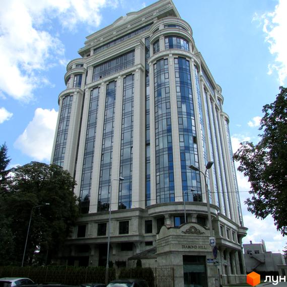 Житловий комплекс Diamond Hill: висока будівля зі світлим фасадом, великими дзеркальними вікнами та вигнутими секціями. Поруч ростуть дерева.