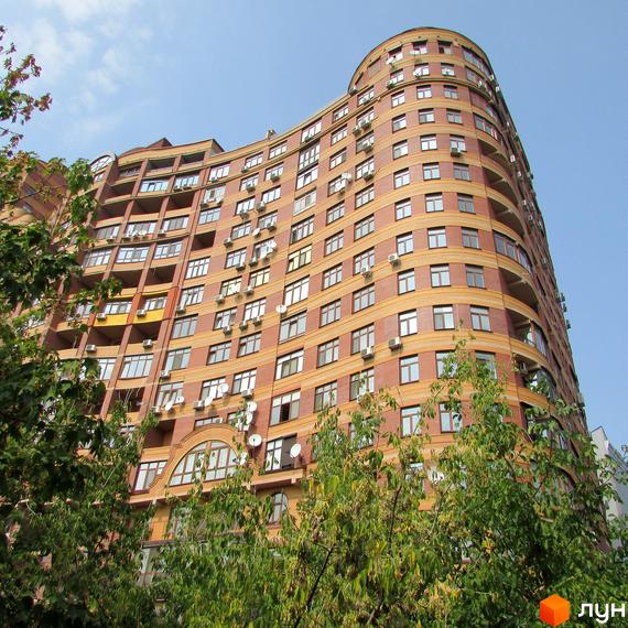 Житловий комплекс на вул. Євгена Коновальця, 36в. Будинок з червоної цегли оточений зеленими насадженнями.