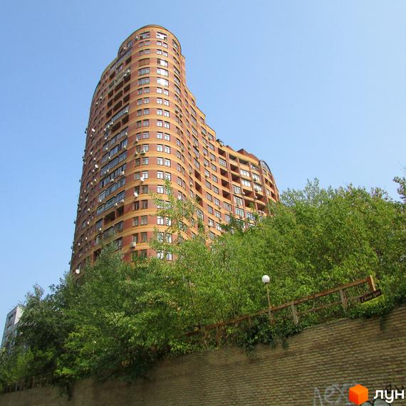 Високоповерховий житловий комплекс на вулиці Євгена Коновальця, 36в. Будинок має вигнуту форму та цегляний фасад. Навколо комплексу зелені насадження та цегляна огорожа.