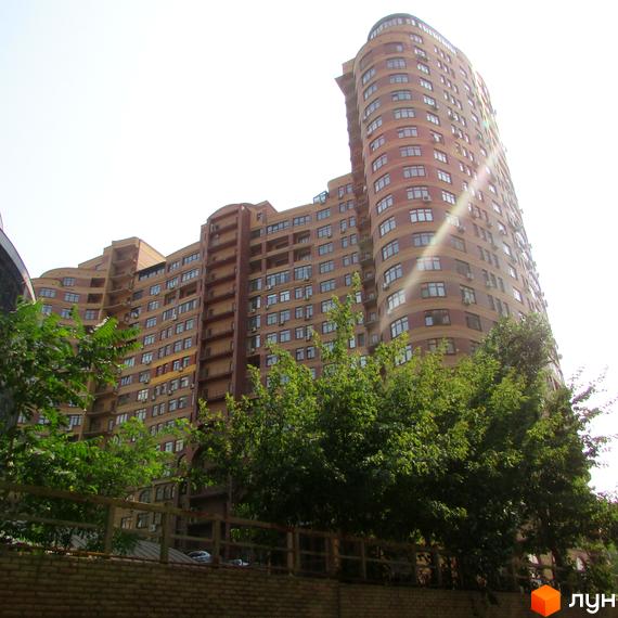 Житловий комплекс на вул. Євгена Коновальця (Щорса), 36в – висотна будівля з вигнутим фасадом та численними вікнами. Перед будинком розташовані дерева та паркан.