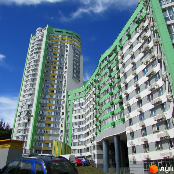 Житловий комплекс Паркове місто: багатоповерхові будинки з хвилястими фасадами зеленого та сірого кольорів. Видно парковку з автомобілями.