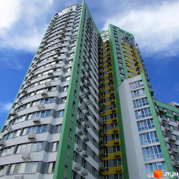 Житловий комплекс Паркове місто: висока багатосекційна будівля з фасадами сірого, зеленого та жовтого кольорів, з великою кількістю вікон.