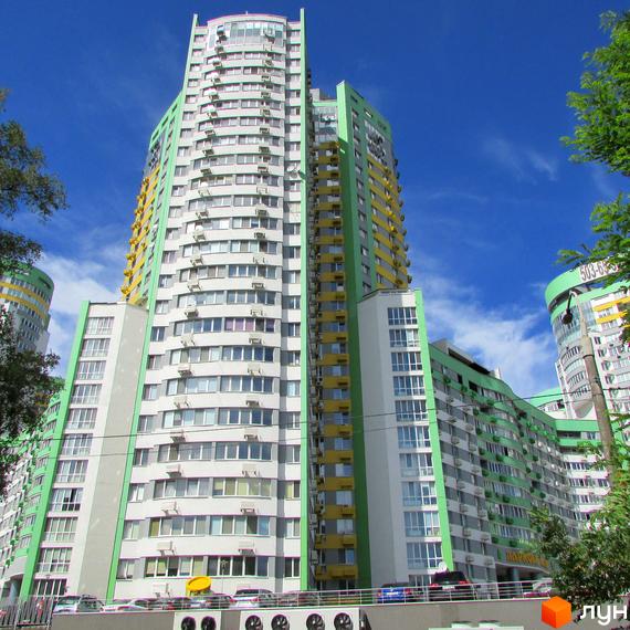 Багатоповерхові будівлі Житлового комплексу Паркове місто з біло-зеленими та жовтими фасадами під блакитним небом. Видно численні вікна, балкони та припарковані автомобілі біля будівель.