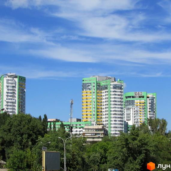 Житловий комплекс Паркове місто з багатоповерховими будинками світло-зеленого, жовтого та білого кольорів. Будинки оточені густою зеленню дерев.