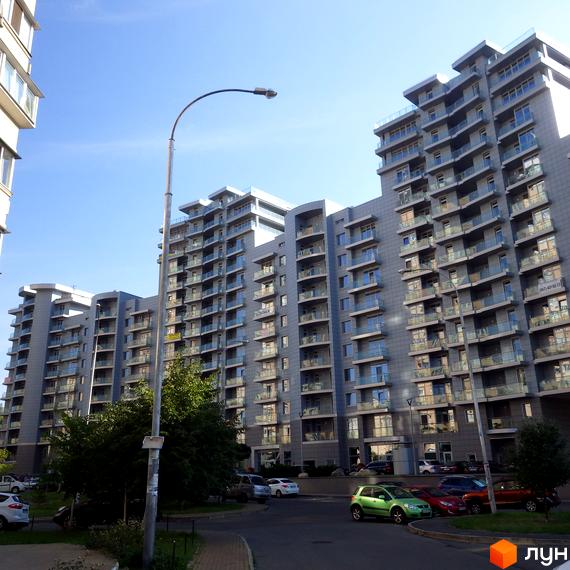 Житловий комплекс Рів'єра Ріверсайд: багатоповерхові будинки з сірим фасадом та скляними балконами, прибудинкова територія з деревами та автомобілями.