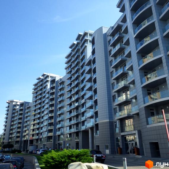 Житловий комплекс Рів'єра Ріверсайд: багатоповерхові будинки з сірим фасадом, скляними балконами та доглянутою прибудинковою територією.