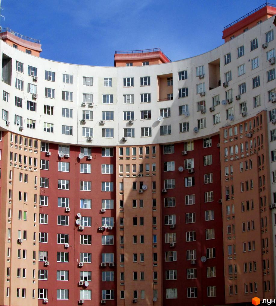 Житловий комплекс Перлина Кадетського Гаю: вигнутий будинок з багатоколірним фасадом, численними вікнами та кондиціонерами.