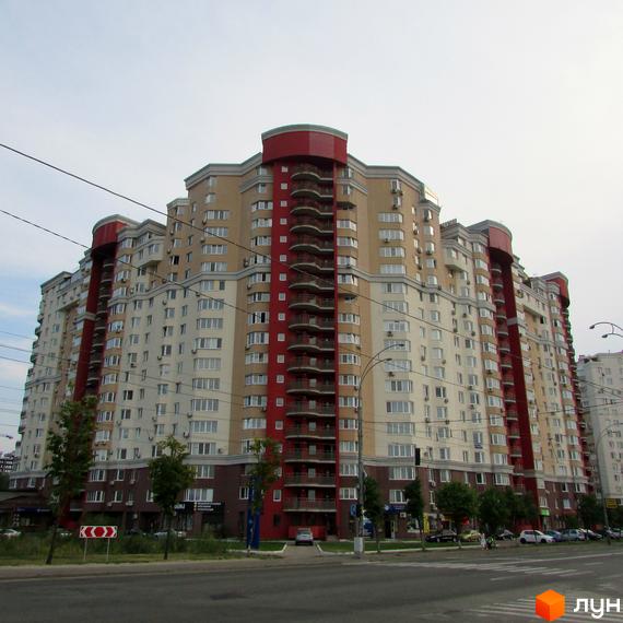 Багатоповерховий житловий комплекс Ліко-Град 3 з бежевими та червоними фасадами. Перед будинком розташована дорога, зелені насадження та припарковані автомобілі.