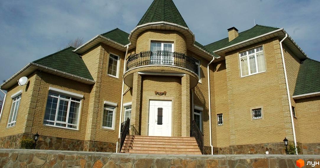 Величний будинок з цегляними стінами та зеленим дахом. Перед будинком камʼяний паркан та сходи до входу.