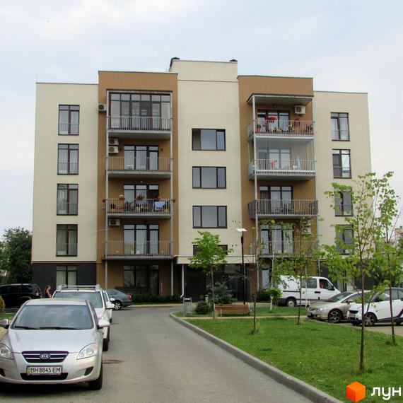 Житловий комплекс Ліпінка: багатоповерховий будинок світло-бежевого та коричневого кольорів з балконами. На прибудинковій території розташовані зелені насадження та припарковані автомобілі.