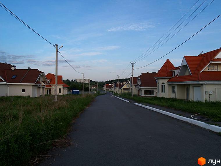 Котеджне містечко Скіфський. Будинки з червоними дахами та світлими фасадами. Поряд дорога та зелені насадження.