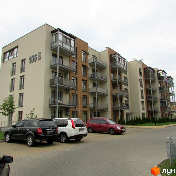 Житловий комплекс Ліпінка з фасадом світло-бежевого кольору та коричневими вставками. Перед будинком розташована парковка з автомобілями.