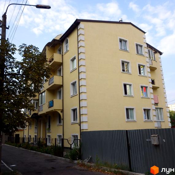 Клубний будинок „Золотий лев“: багатоповерхова будівля світло-жовтого кольору з білими кутовими елементами та балконами. Перед будинком дорога та металевий паркан.