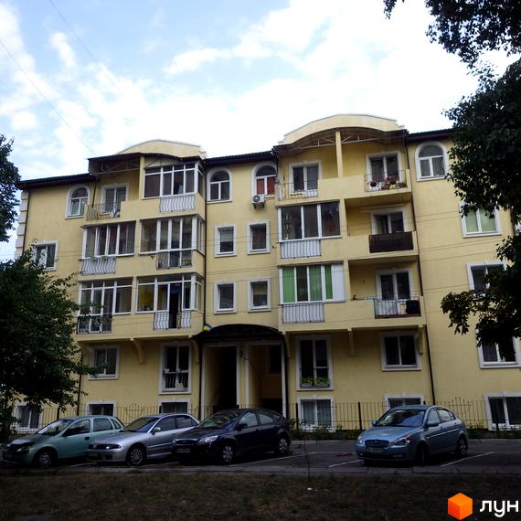 Клубний будинок „Золотий лев“ з жовтою фасадною обробкою та балконами. Прибудинкова територія з автомобілями та зеленими насадженнями.