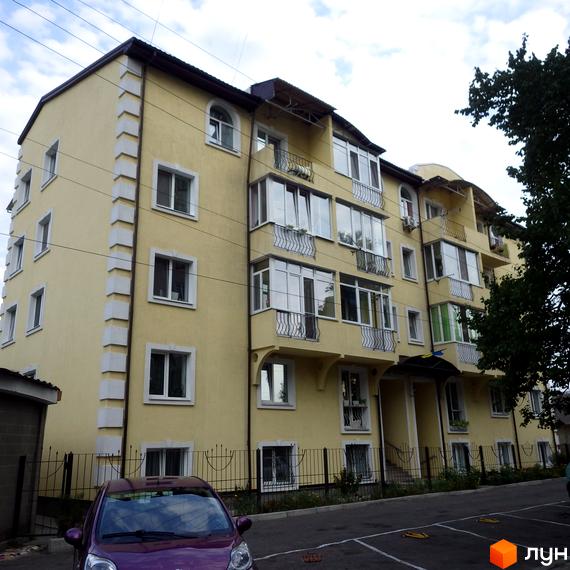 Житловий комплекс Золотий лев з жовтою фасадною стіною та балконами. Прибудинкова територія з паркувальними місцями та зеленими насадженнями.