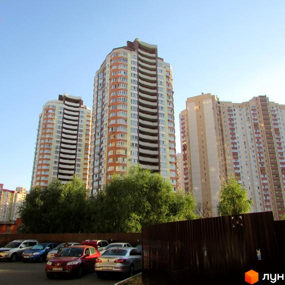 Житловий комплекс на вул. Ахматової, 34, з висотними будинками та прибудинковою територією з зеленими насадженнями і паркувальними місцями.