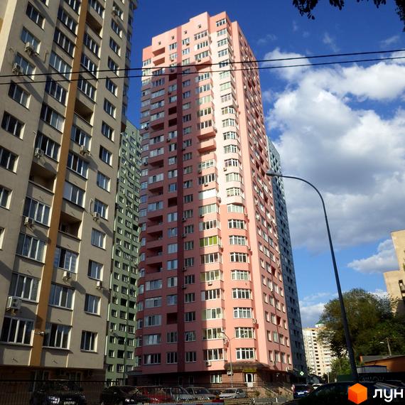 Житловий комплекс на вул. Феодосійській, 2: висока рожева багатоповерхівка, поруч сірі будинки. Видно прибудинкову територію з автомобілями.