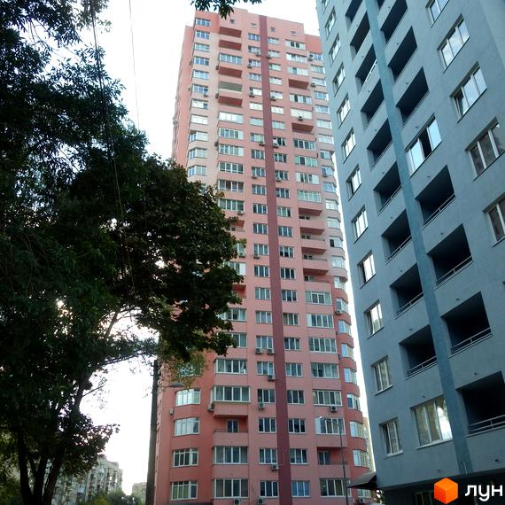 Багатоповерхові житлові будинки рожевого та світло-сірого кольорів з балконами та вікнами. Житловий комплекс на вул. Феодосійська, 2, оточений зеленню.