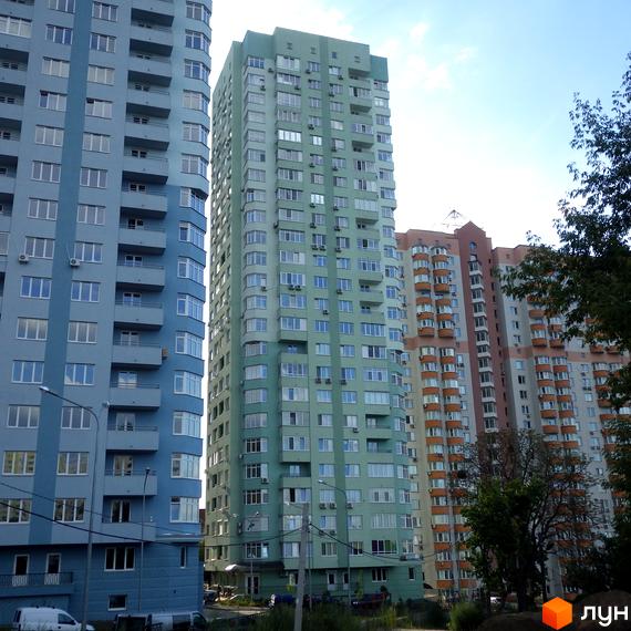 Житловий комплекс на вул. Феодосійська, 2 з трьох багатоповерхових будинків синього, зеленого та коричневого кольорів. Видно балкони, вікна та дерева.