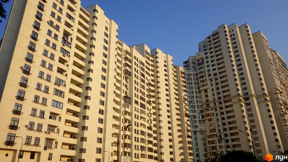 Високі світлі будівлі Житлового комплексу Панорама на Печерську з численними вікнами та балконами, розташовані під чистим блакитним небом.