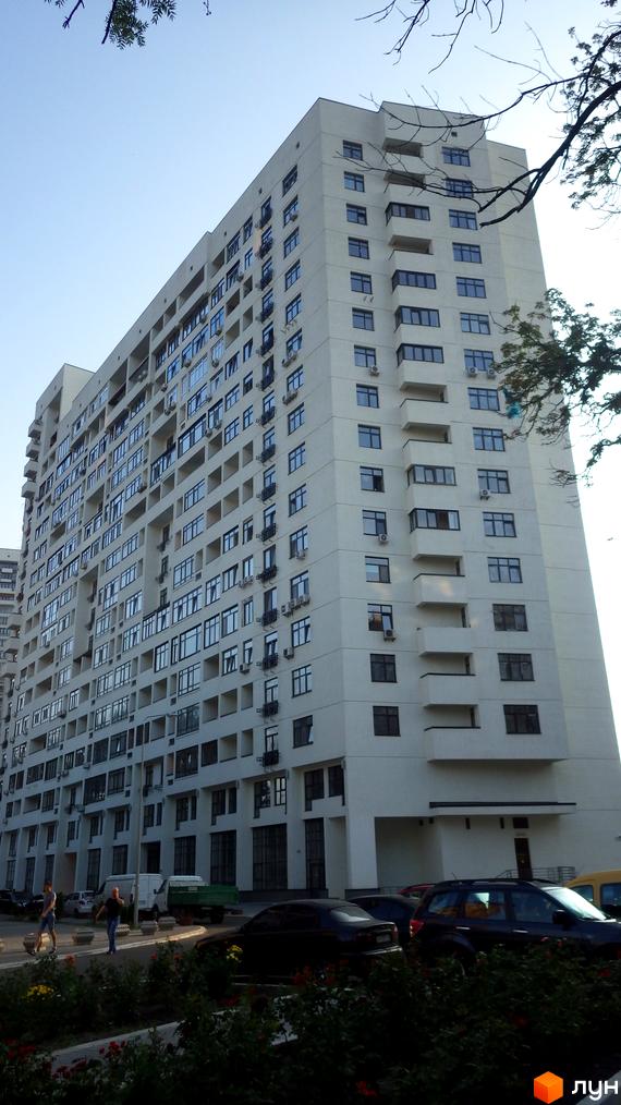 Багатоповерховий житловий комплекс Панорама на Печерську світлого кольору з вікнами та балконами. Поруч зелені насадження та автомобілі.