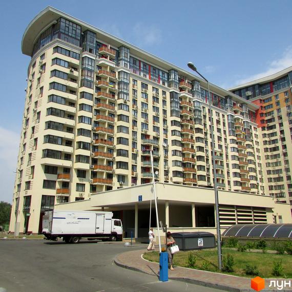 Житловий комплекс Сонячна брама: багатоповерховий будинок світлого кольору з численними балконами та вигнутим дахом. На передньому плані – дорога та вхідна група.