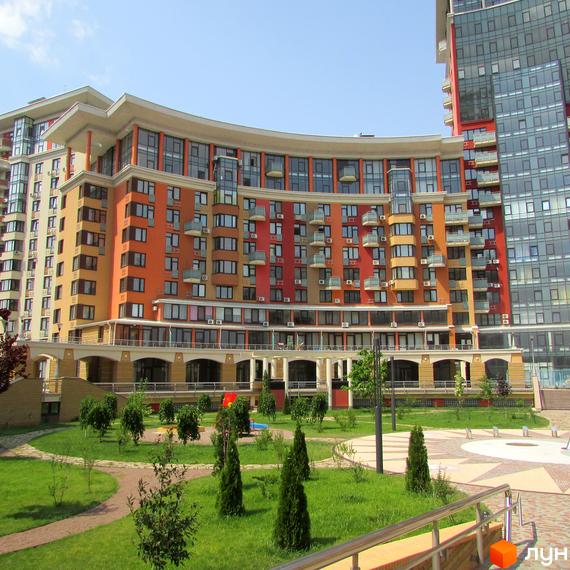 Житловий комплекс Сонячна брама має вигнутий фасад у помаранчевих та червоних тонах. На передньому плані – зелений двір з деревами та доріжками.