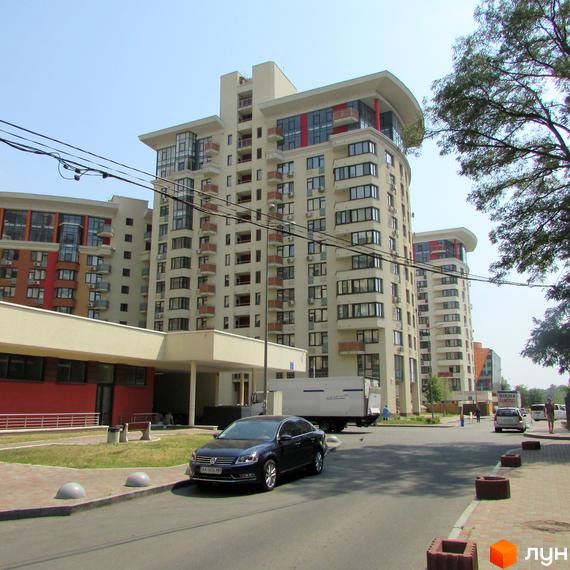 Житловий комплекс Сонячна брама: багатоповерхові будинки світлого кольору з балконами та великими вікнами. На передньому плані дорога та зелені насадження.