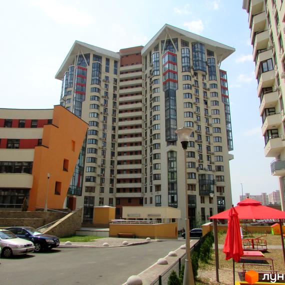 Багатоповерховий будинок Житлового комплексу Сонячна брама зі світлим фасадом, балконами та скляними елементами. На прибудинковій території видно дитячий майданчик та парковку.