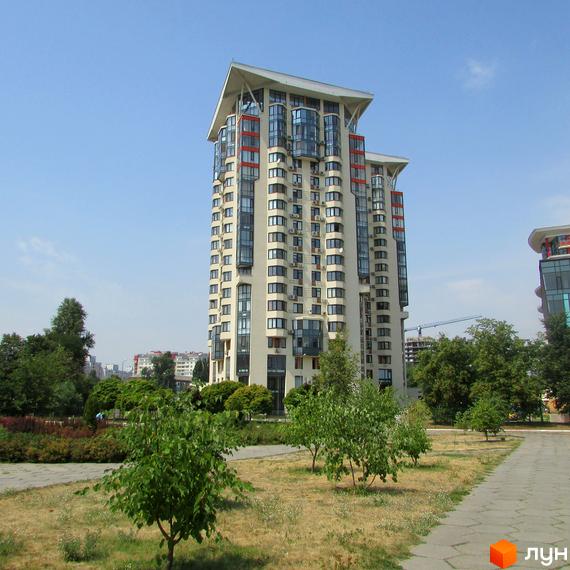 Житловий комплекс Сонячна брама – висотна будівля світлого кольору з численними вікнами та балконами. Навколо зелені дерева, трав'яні ділянки та доріжки.