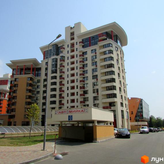 Багатоповерховий будинок Житлового комплексу Сонячна брама з балконами та червоними елементами. Перед будинком розташована автомийка та в'їзд до підземного паркінгу.