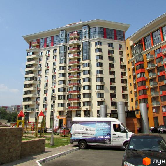 Багатоповерховий будинок Житлового комплексу Сонячна брама з бежевим фасадом та червоними балконами. Поруч розташований дитячий майданчик та паркувальна зона.