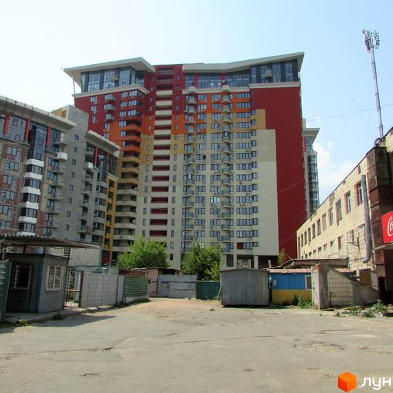 Житловий комплекс Сонячна брама: багатоповерхова будівля з різнокольоровим фасадом та балконами. На передньому плані – ділянка з господарськими спорудами.