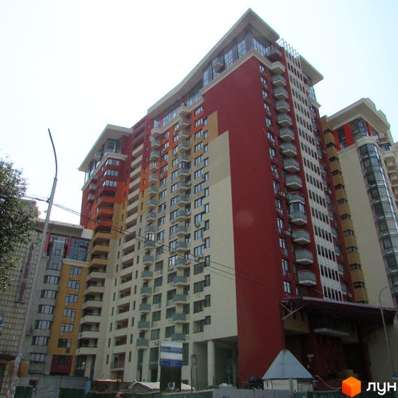 Житловий комплекс Сонячна брама: багатоповерховий будинок з фасадами червоного, помаранчевого та світлого кольорів, обладнаний балконами. На передньому плані будівельний майданчик.