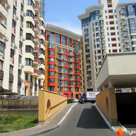 Багатоповерхові будинки Житлового комплексу Сонячна брама з білими, помаранчевими та червоними фасадами. Дорога веде до підземного паркінгу.