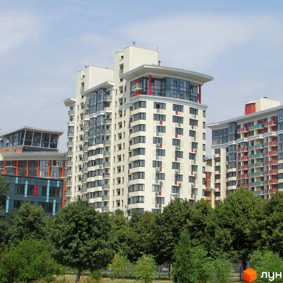 Житловий комплекс Сонячна брама: багатоповерхові будинки світлого кольору з балконами та скляними фасадами. Навколо зелені дерева та доглянута територія.