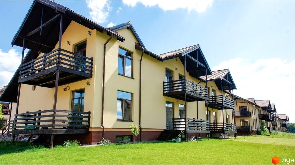 Котеджний комплекс Садок Вишневий. Двоповерхові будинки з балконами та терасами. Зелена трава та блакитне небо з хмарами.