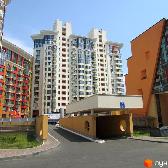 Житловий комплекс Сонячна брама: багатоповерховий будинок світлого кольору з балконами та великими вікнами. На передньому плані в'їзд до підземного паркінгу.