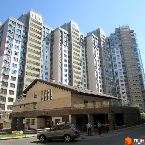 Багатоповерхові будинки Житлового комплексу Новопечерські Липки з балконами та численними вікнами. На передньому плані видно прибудинкову споруду та дорогу з автомобілем.