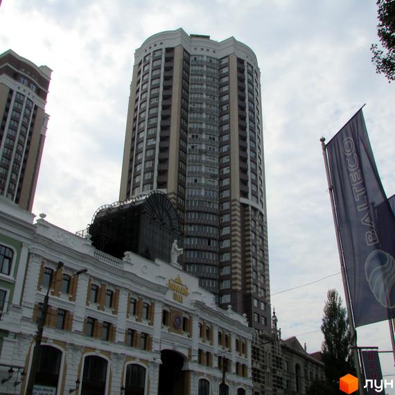 Багатоповерховий Житловий комплекс Покровський посад з фасадом світлих та темних відтінків, численними вікнами та балконами. Перед ним розташована будівля з класичною архітектурою.