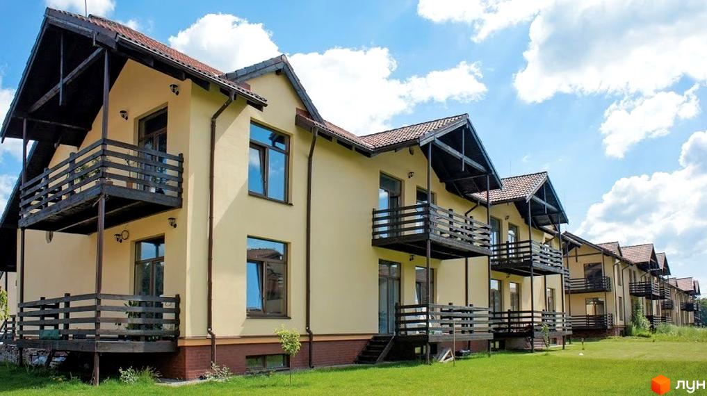 Котеджне містечко Садок Вишневий. Двоповерхові будинки з балконами та коричневою черепицею на даху. На території зелена трава та блакитне небо з хмарами.