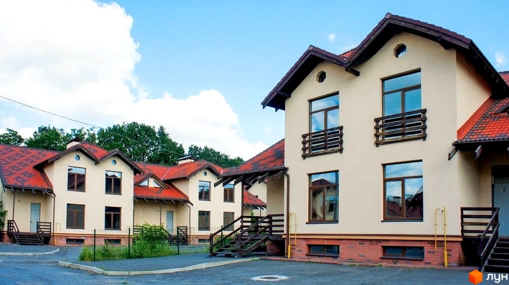 Зображення житлового будинку з червоним дахом та світлими стінами. На передньому плані видно сходи та невелику прибудинкову територію з асфальтом.