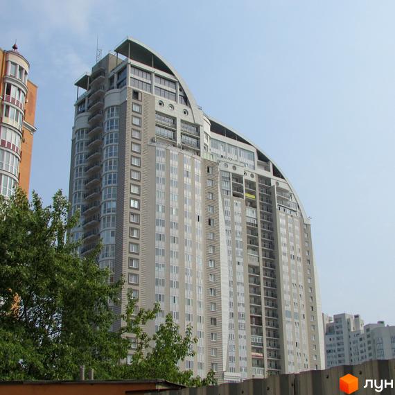 Багатоповерховий житловий комплекс на просп. Володимира Івасюка (Героїв Сталінграда), 2, має світлі фасади та вигнутий дах. Частина будівлі закрита деревами.